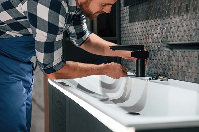 Professional plumber installing a modern faucet in a newly renovated bathroom.